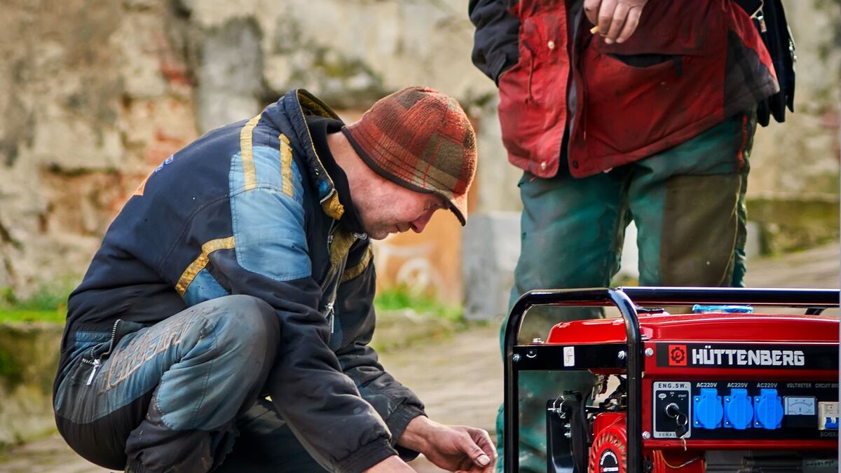 Two men crouched beside a red portable generator, checking it before starting it up