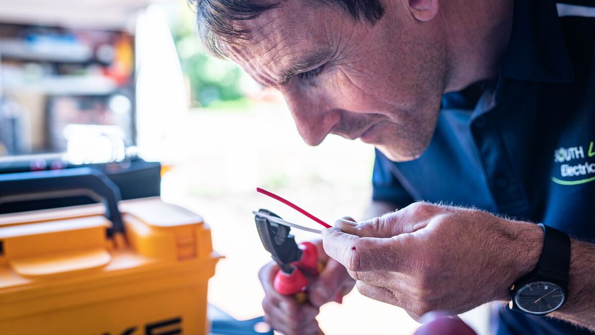 An electrician stripping the insulation from a wire with pliers beside an open tool case