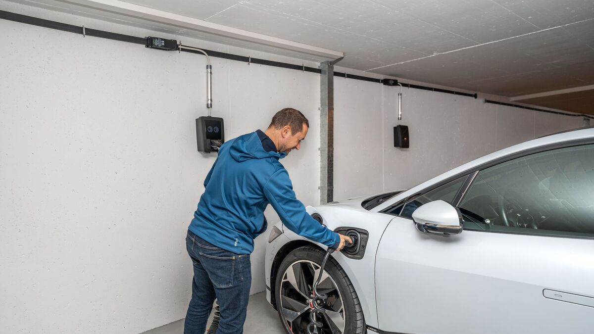 A man plugging a white electric car into a wall-mounted charger inside a home garage