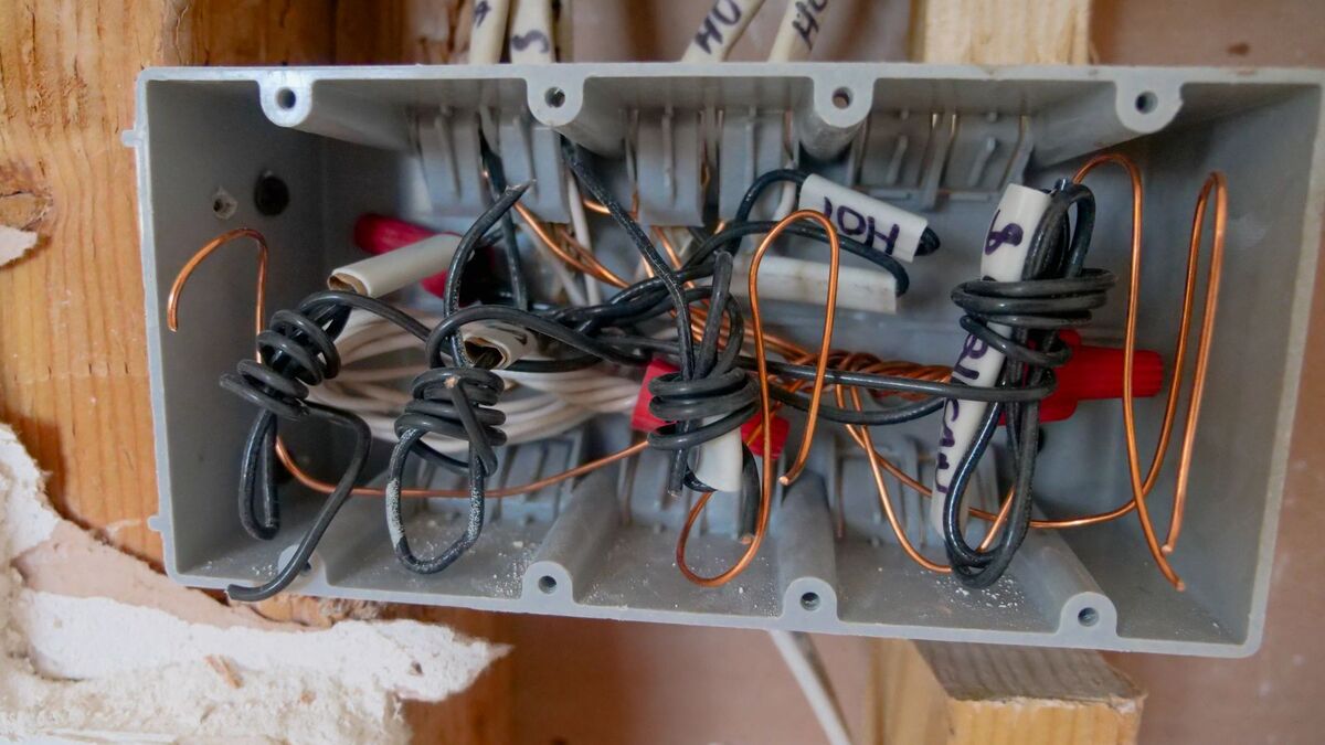 An open junction box packed with wires inside an unfinished wall during rewiring work