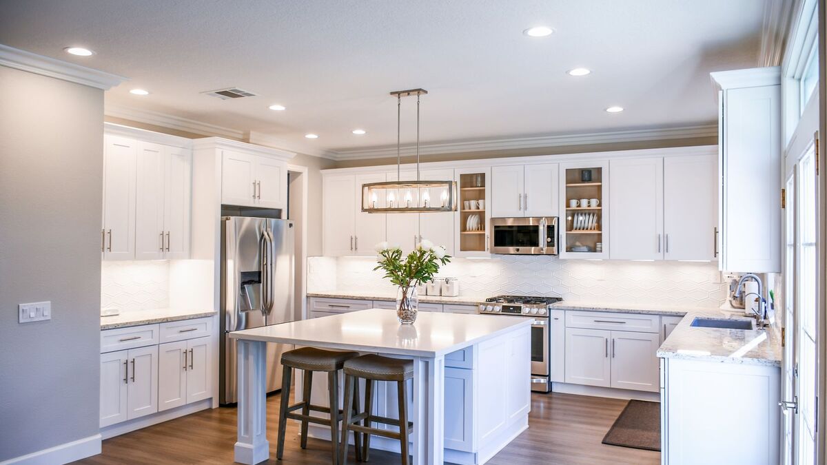 A bright white kitchen with recessed ceiling lights and a pendant fixture over the island