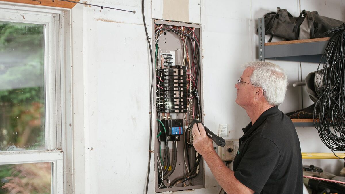 An electrician working at an open residential breaker panel mounted on a wall
